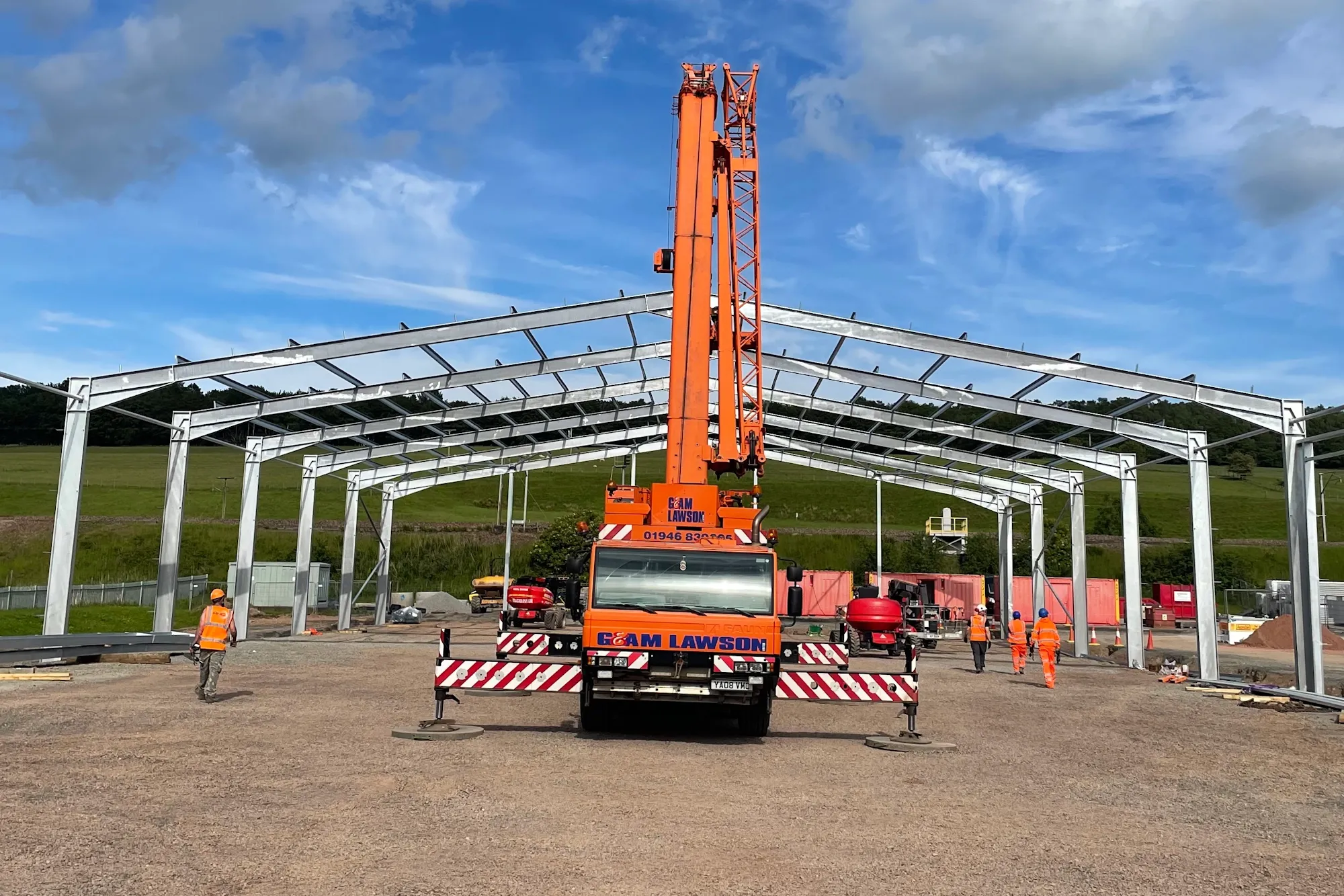 Large steel frame of a building being erected by a crane under a blue sky